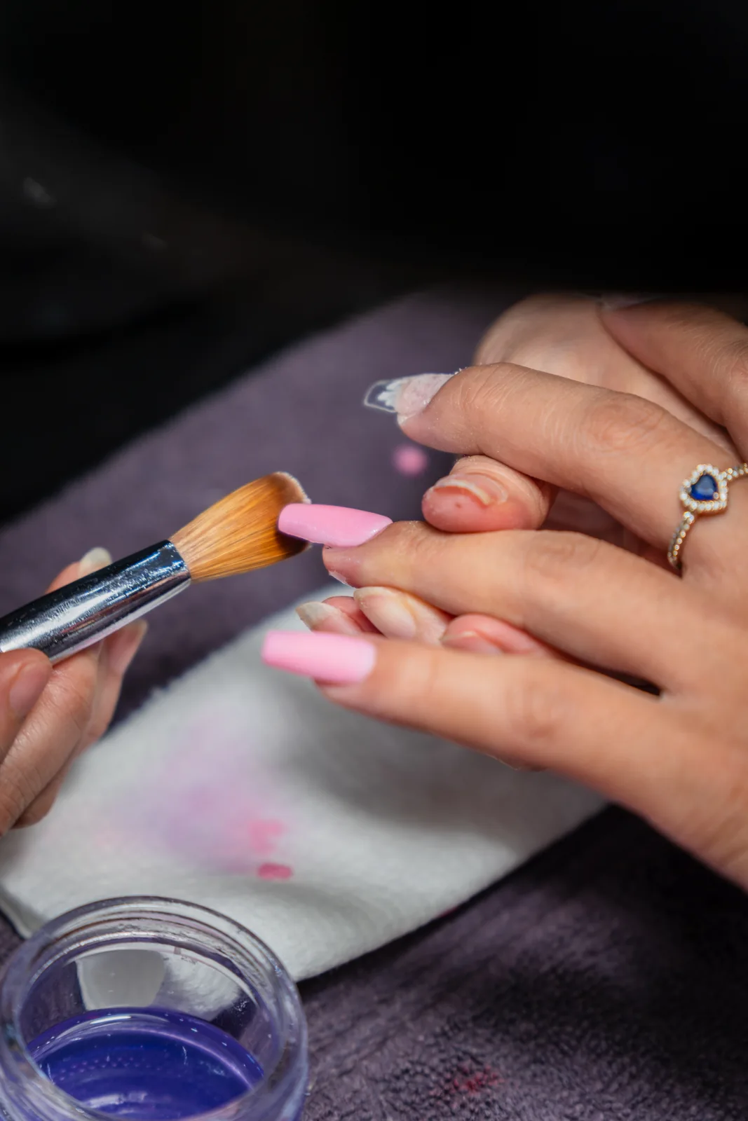 A brush shaping pink acrylic on a nail in close-up